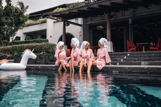 Group of four fashionable and elegance women weating the same clothes posing near the swimming pool. Concept of friendship. Casual lifestyle