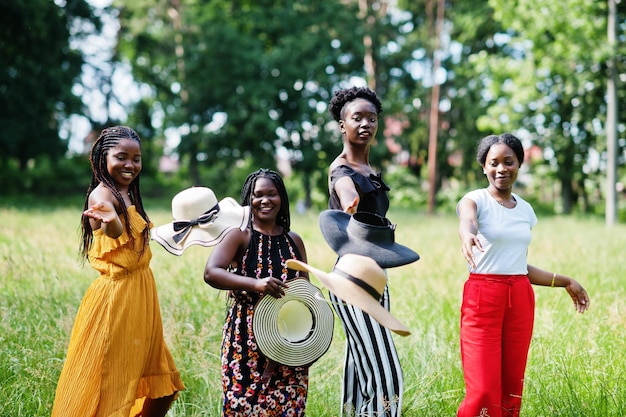 4명의 멋진 아프리카계 미국인 여성 그룹이 공원의 푸른 잔디에서 시간을 보내는 여름 모자를 쓰고 있습니다.