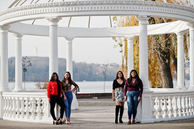 Group of four happy and pretty latino girls from Ecuador posed at street against ancient arch.