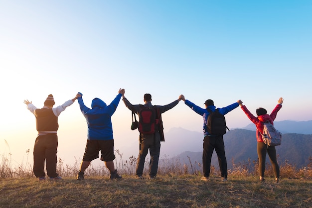 Group of four people stands on the top of mountain in winner pose. Team or teamwork succes