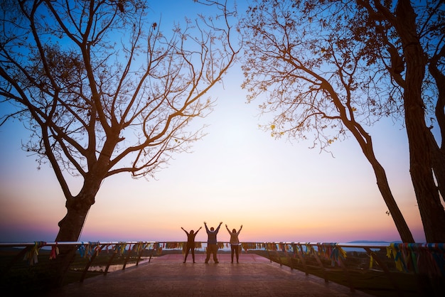 Group of four people stands on the top of mountain in winner pose.