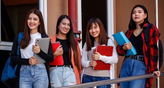 Photo group of four young attractive asian girls college students standing together in university campus smiling and with joy. concept for education and college students life.