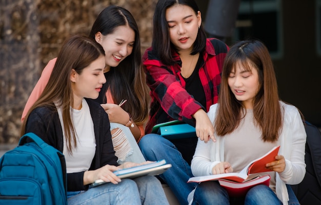 대학 캠퍼스 야외에서 함께 공부하는 4명의 매력적인 아시아 여자 대학생 그룹. 교육, 우정, 대학생들의 삶에 대한 개념.