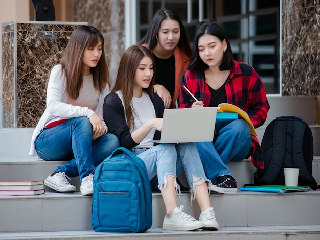 Group of four young attractive asian girls college students studying together using laptop in university campus outdoor. Concept for education, friendship and college students life.