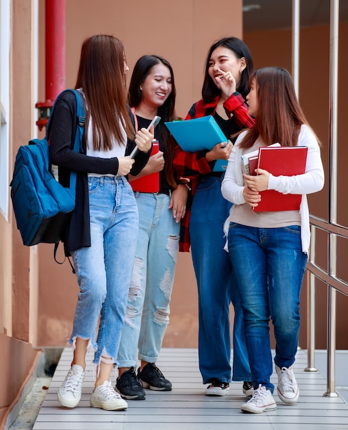 Un gruppo di quattro giovani studenti universitari attraenti ragazze asiatiche che camminano insieme nel campus universitario parlando e ridendo di gioia. concetto per l'istruzione e la vita degli studenti universitari.