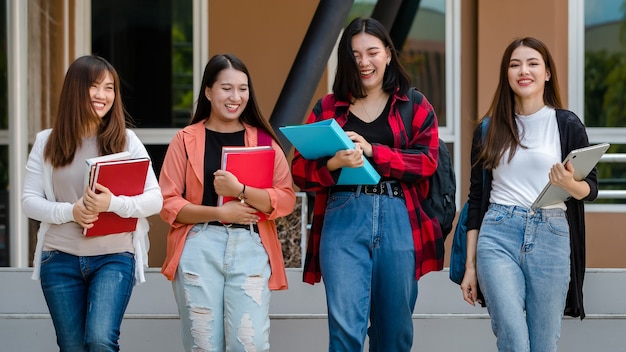 Group of four young attractive asian girls college students walking together in university campus talking and laughing with joy. Concept for education and college students life.