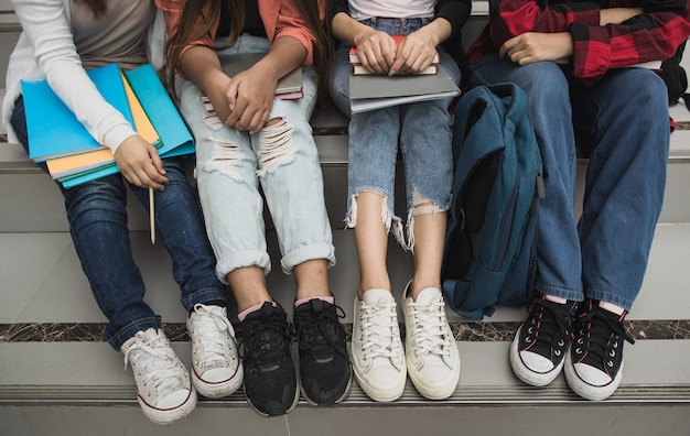 屋外の大学のキャンパスで一緒に座っている4人の若い女の子の大学生の脚とスニーカーのグループ。教育、友情、大学生の生活のための概念。