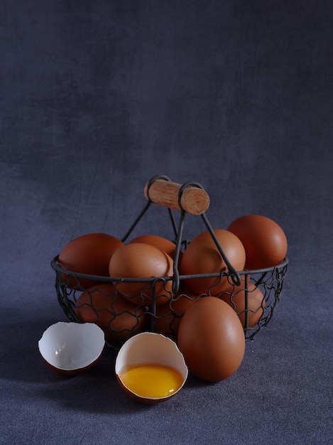 A group of fresh eggs in rustic iron basket with split egg and yolk on grey base and background.