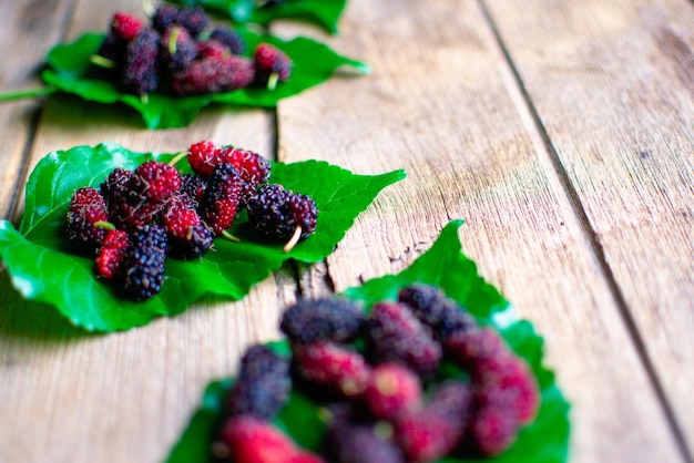 Group of fresh mulberries on green leaves against wooden background