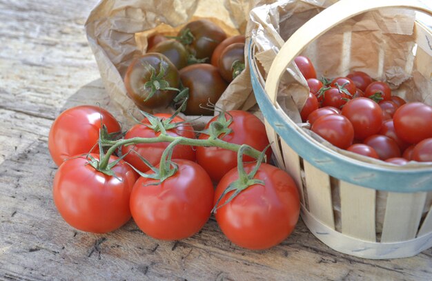 Group of fresh tomatoes in crate and basket on a wooden table