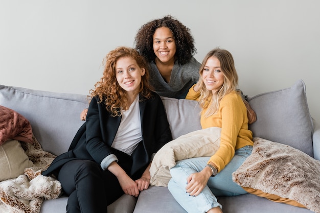 Group of friendly intercultural girls in smart casual sitting on sofa