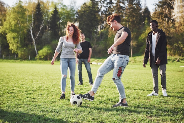 カジュアルな服装で友達のグループが屋外でサッカーをします。人々は楽しんで、楽しんでいます。アクティブな休息と美しい夕日