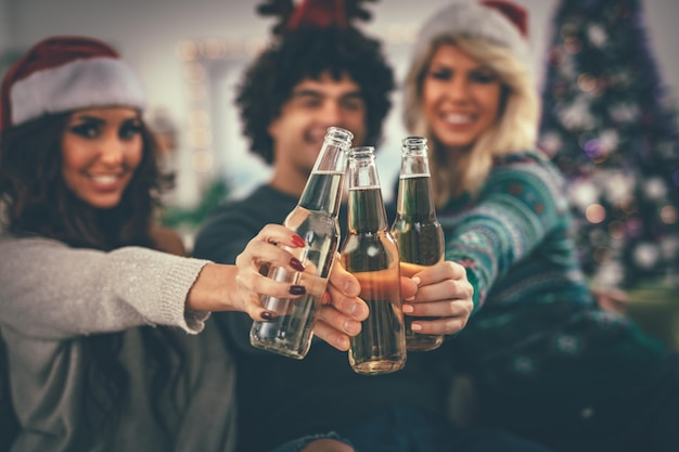 Group of friends celebrating Christmas at home, they are having fun and toasting with beer. Selective focus.