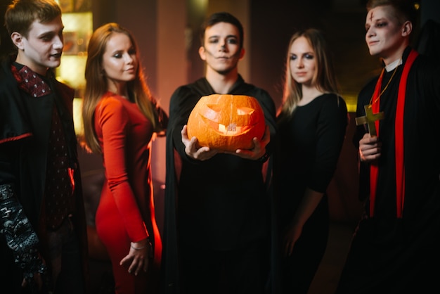 Photo group of friends celebrating halloween guy wearing bat costume holds pumpkin