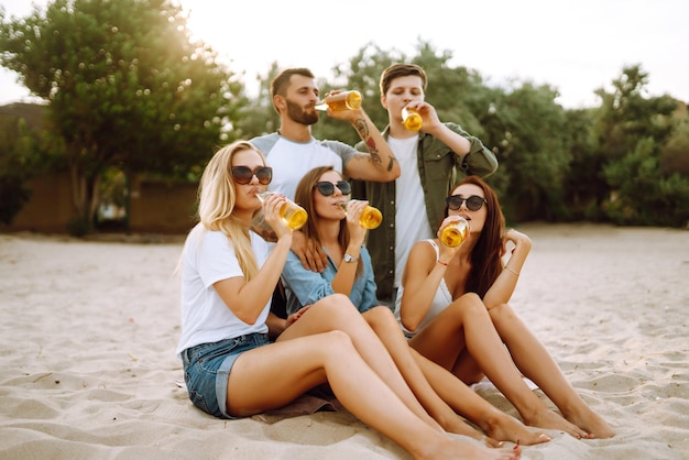 Group of friends cheers and drink beers on beach Young friendsrelaxing and having picnic Suummertime