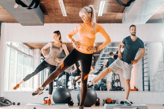 Group of friends doing fitness exercises for legs in gym. In background their mirror reflection.