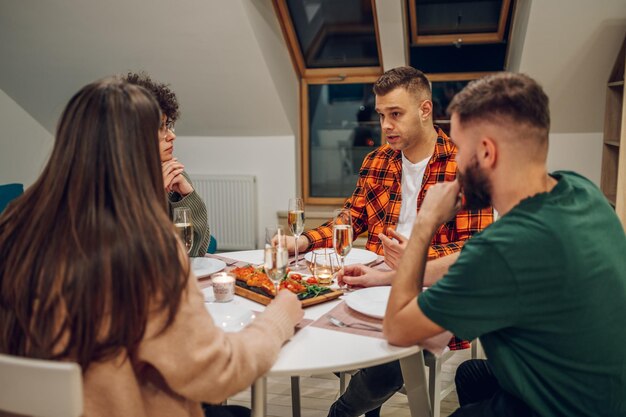 Group of friends enjoying dinner while sitting at the kitchen table together