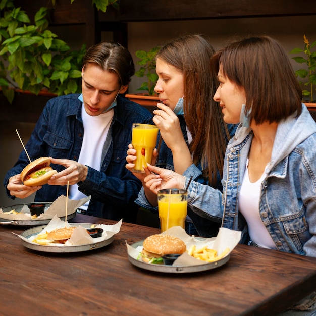 Gruppo di amici che mangiano hamburger con patatine fritte e succo di frutta