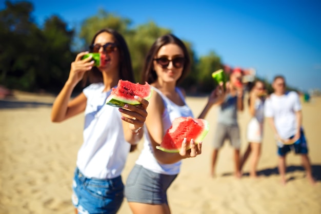 Group of friends having fun eating watermelon on the beach Excellent sunny weather Super mood Summer