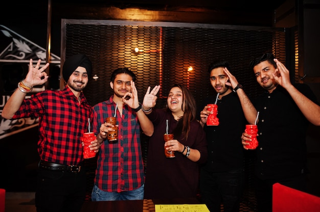 Group of friends having fun and rest at night club, drinking cocktails and show ok fingers together