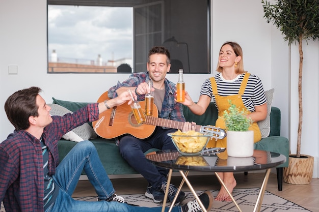 Group of friends having some beers and playing the guitar together at home Concept lifestyle music friendship