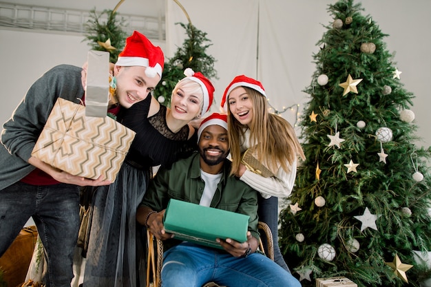  group of friends holding present boxes and celebrating Christmas at decorated home