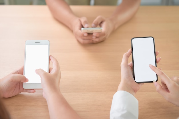 Group of friends holding smartphone with blank screen on table in cafe.