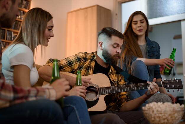 Group of friends on a house party playing guitar and enjoying music