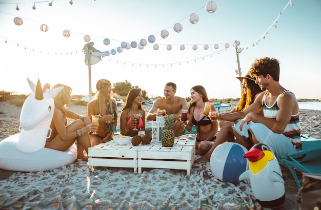 Group of friends making party on the beach at sunset time