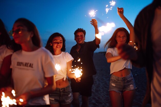 Group of friends at night on the beach with sparklers Young friends enjoying on beach holiday