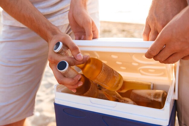 Gruppo di amici all'aperto sulla spiaggia che tengono le scatole con la birra