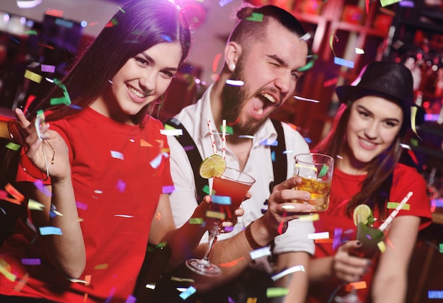 A group of friends at a party in a nightclub clink glasses with alcoholic beverages.