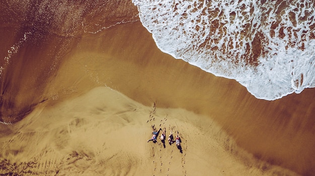 Group of friends people enjoying the beach laying on the sand  aerial top view with waves connig summer vacation travel lifestyle for young men and women during holiday  coloured landscape vertical