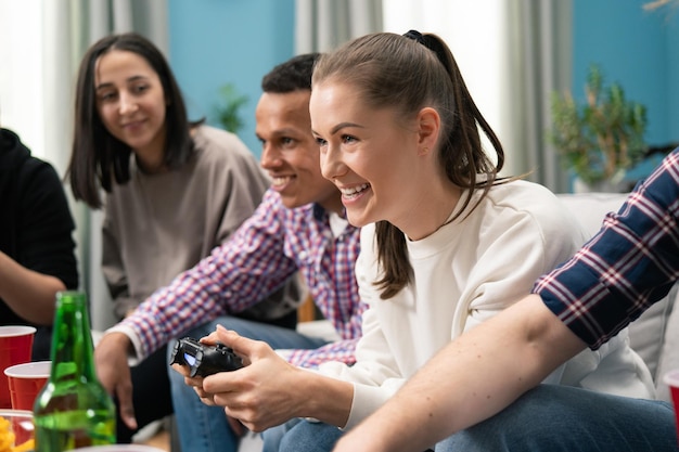 Group of friends play video games together at home having fun a smiling woman competes with a friend