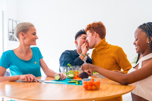 Group of friends preparing vegetarian food Preparing the salad and having fun in the kitchen lgtb boy couple kiss with carrot