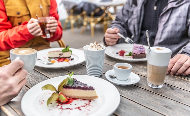 A group of friends on a restaurant terrace in winter during Quarantine Covid-19. Cheesecakes and hot coffees enjoyed by friends sitting around the cafe house table.