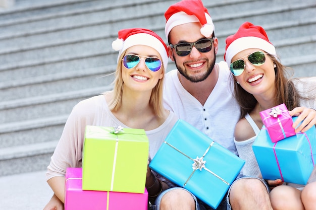 group of friends in Santa's hats sitting in the city with presents