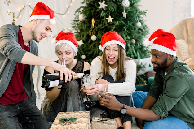 Group of friends sitting next to Christmas tree and drinkink chapmagne