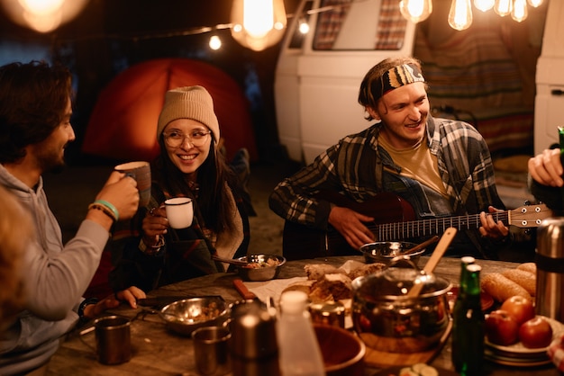 Foto gruppo di amici seduti a tavola e suonare la chitarra la sera durante un picnic all'aperto