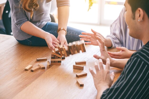 Группа друзей сидит и играет в игру с деревянными блоками Tumble tower вместе с чувством счастья