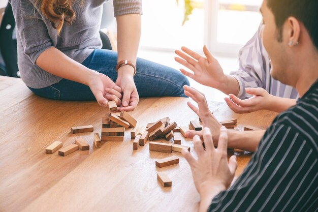 Группа друзей сидит и играет в игру с деревянными блоками Tumble tower вместе с чувством счастья