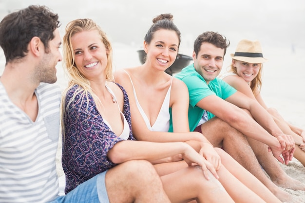 Foto gruppo di amici seduti fianco a fianco sulla spiaggia