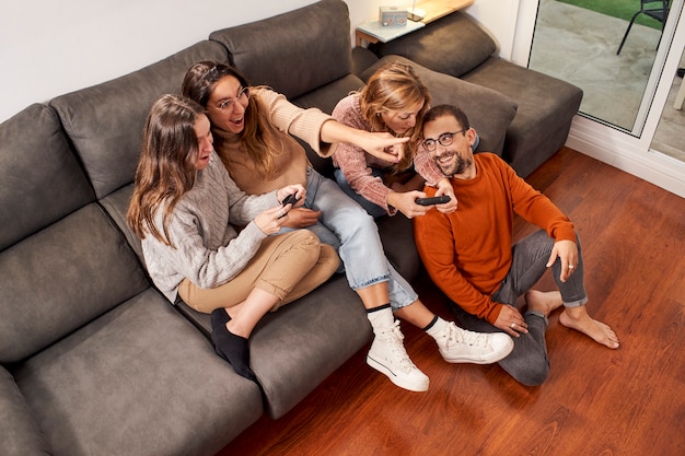 Group of friends sitting on sofa in living room and playing video games at home