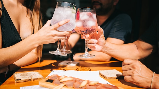 Group of friends sitting on the terrace in summer toast together with cocktails and a snack