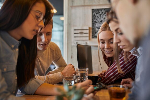 Group of friends sitting together in a cafe sharing smartphone