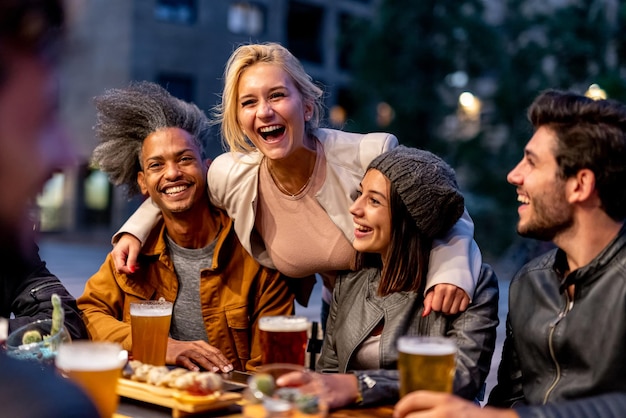 Group of friends smiling and drinking at brewery meeting of couple of millennials toasting with beers and eating fusion food nightlife and social gathering of young people after covid19 outbreak