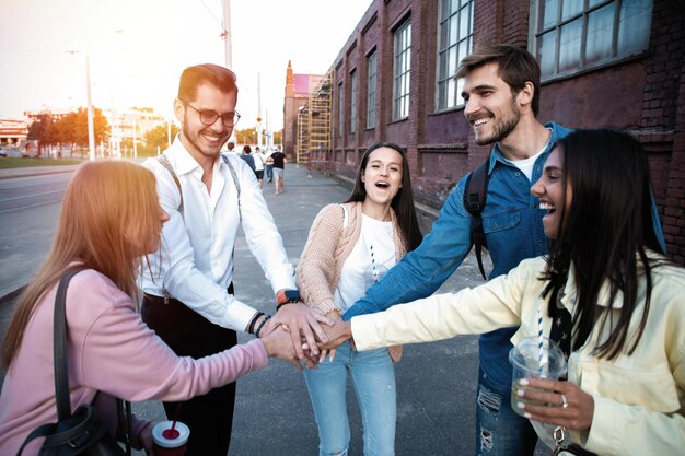 Foto gruppo di amici che impilano le mani all'aperto giovani felici che si divertono unendosi e festeggiando insieme