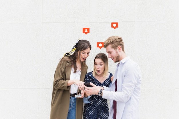 Photo group of friends standing near the wall texting on mobile phone