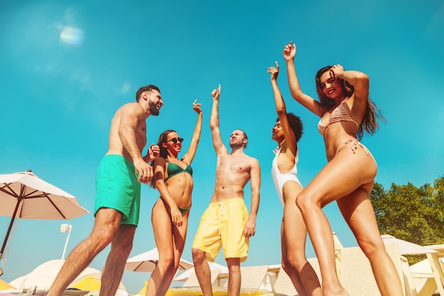 Group of friends in swimsuit dance music in a swimming pool