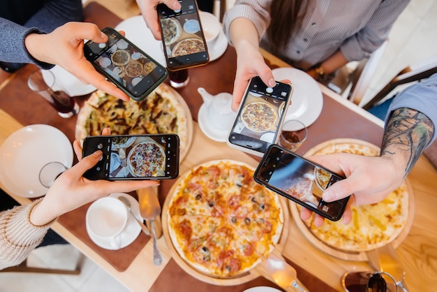 Группа друзей делает фото вкусной пиццы крупным планом для блога pizzeria